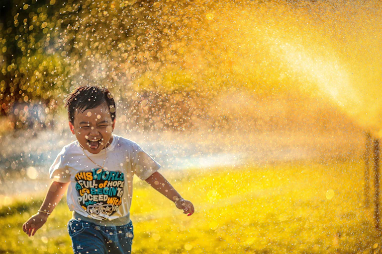A little boy runs through a sprinkler in bright golden sunshine