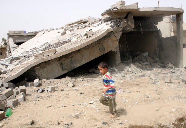 A boy runs past a damaged house.