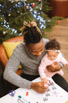 A father holds a baby on his knee while drawing with coloured pens