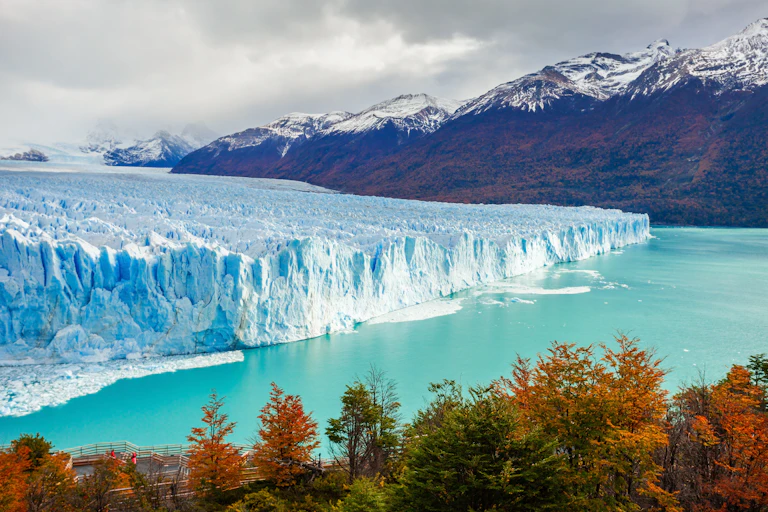 A blue glacier surrounded by mountains and forest.