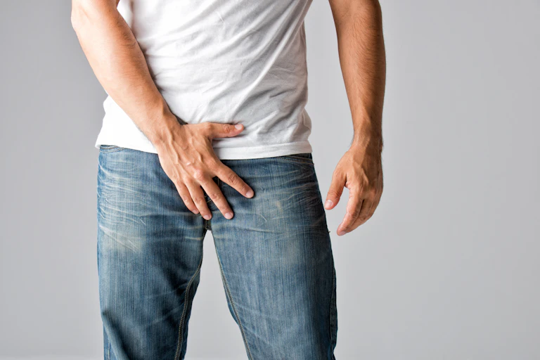 Un homme avec sa main sur son pantalon, à la hauteur de son pénis