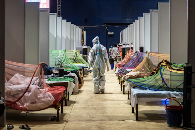 Patients are lined up in a beds and a medical worker in full protective gear walks past them.