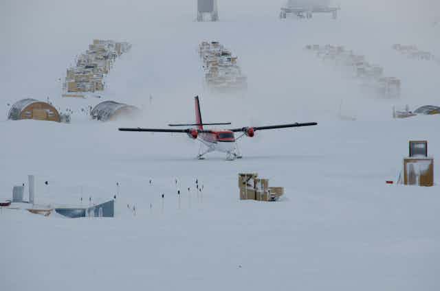 A light aircraft lands on a snow field at the South Pole with boxes of supplies