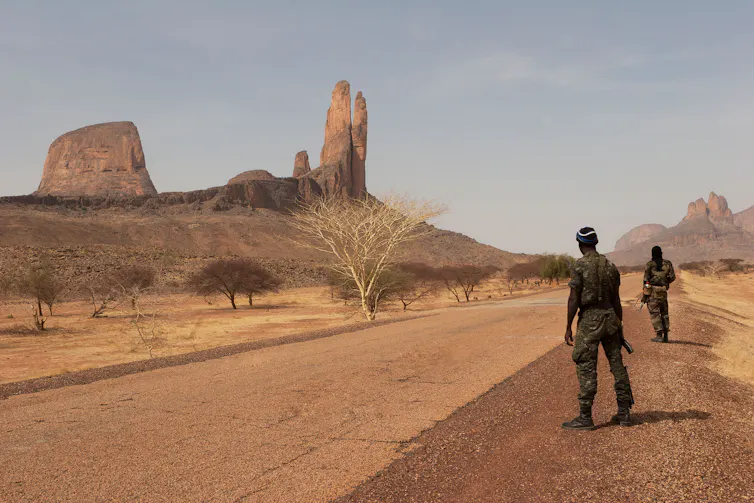 Armed soldiers patrol an empty road in barren countryside in central Mali
