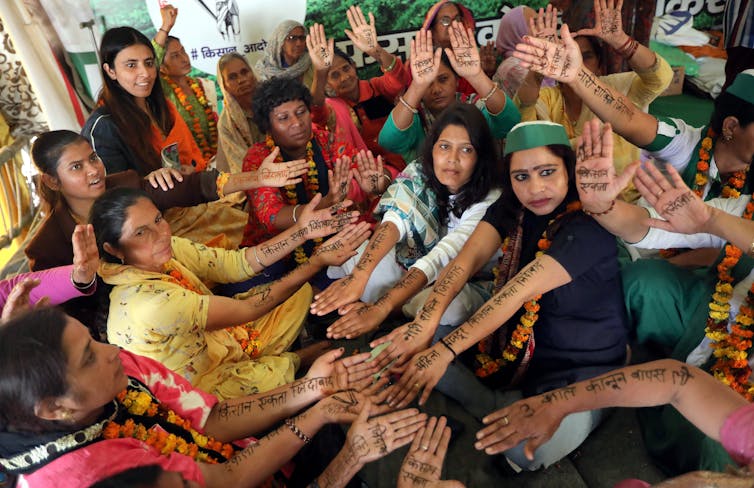 Indian women farmers and activists show their hands with pro-farmer and -women slogans written with henna in Hindi.
