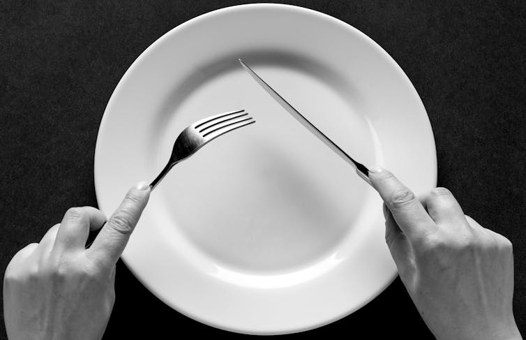 An image of two hands holding a knife and fork over an empty plate.