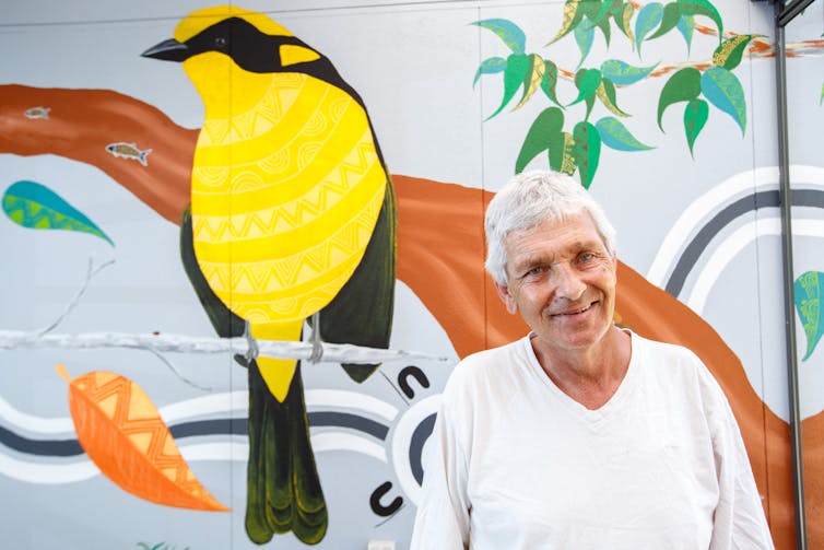 Man with bird mural on wall behind him