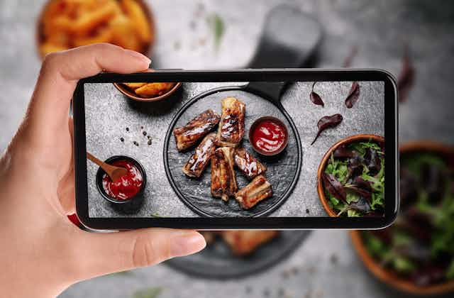 A hand taking a photo of a dish of ribs