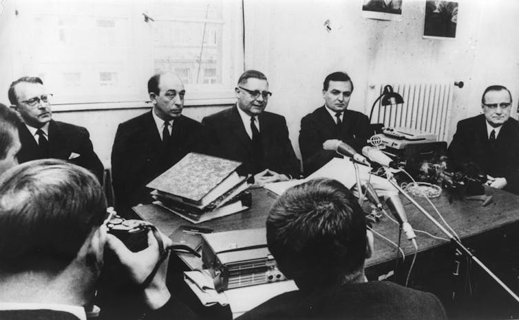 Black and white photo of men crowded around a conference table.