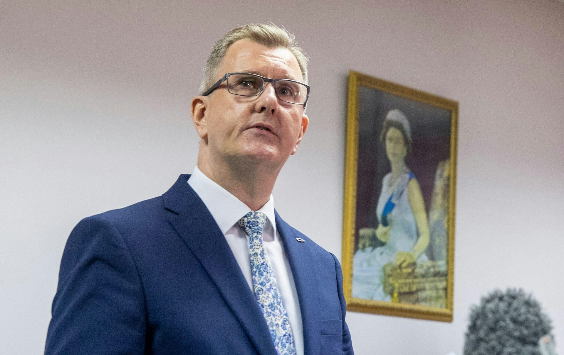 Jeffrey Donaldson giving a press conference in front of a portrait of the Queen.
