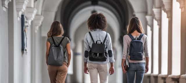 Three students walk along a corridor.