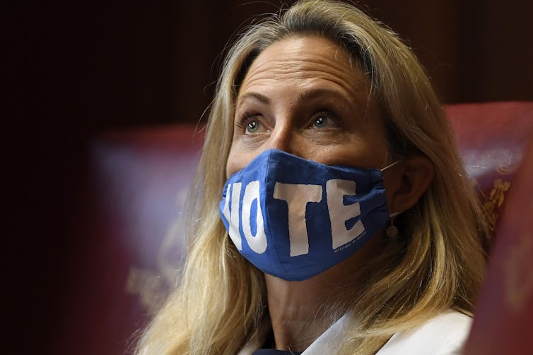 Una mujer mirando hacia arriba con una máscara azul con la palabra 'VOTE'.