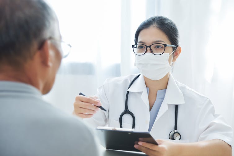 A family doctor in a face mask talking to a patient