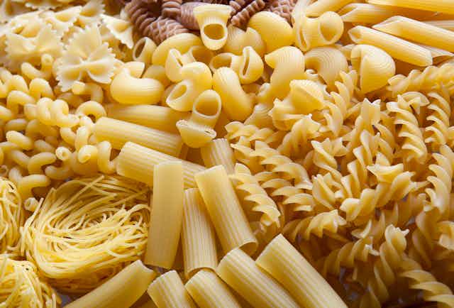 Various pasta shapes including elbow macaroni and spirals lie next to each other 