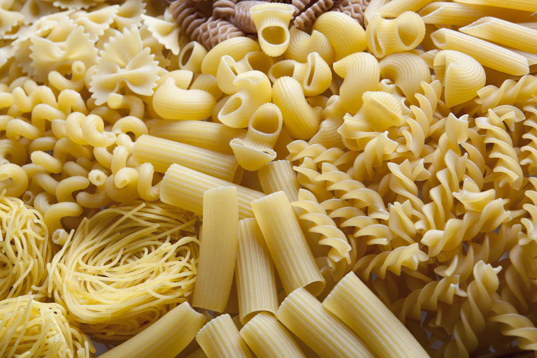 Various pasta shapes including elbow macaroni and spirals lie next to each other