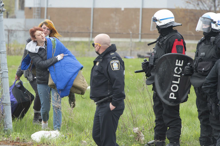 People carry their supplies as police usher them out of tent camp