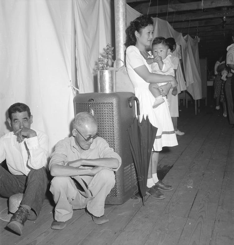 Two men squat near a stove, with a woman holding a child