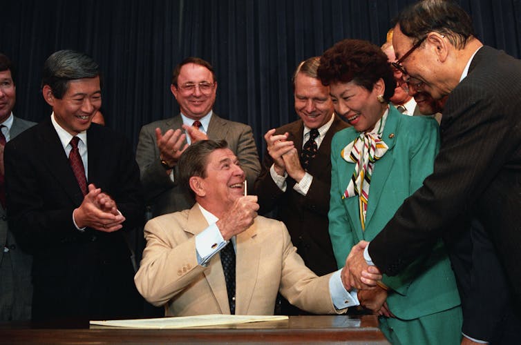 Ronald Reagan, sitting, shakes hands with smiling people
