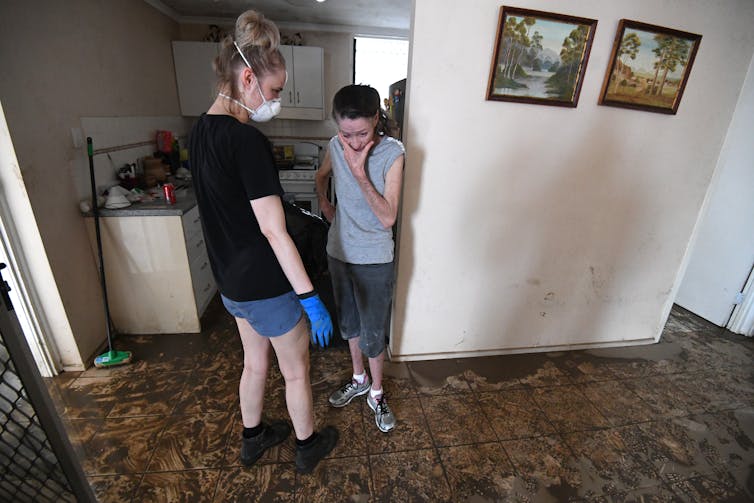 A woman looks at her flood-damaged house