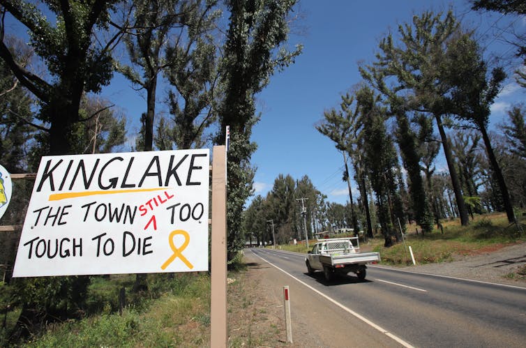 A sign outside a fire affected town says 'Kinglake, the town still too tough to die'.