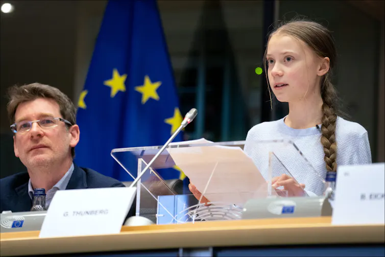 A young woman speaks into a microphone as she reads from a lectern