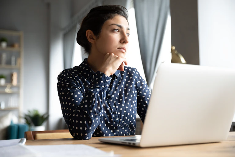 A woman sitting in front of a laptop looking away from the screen.