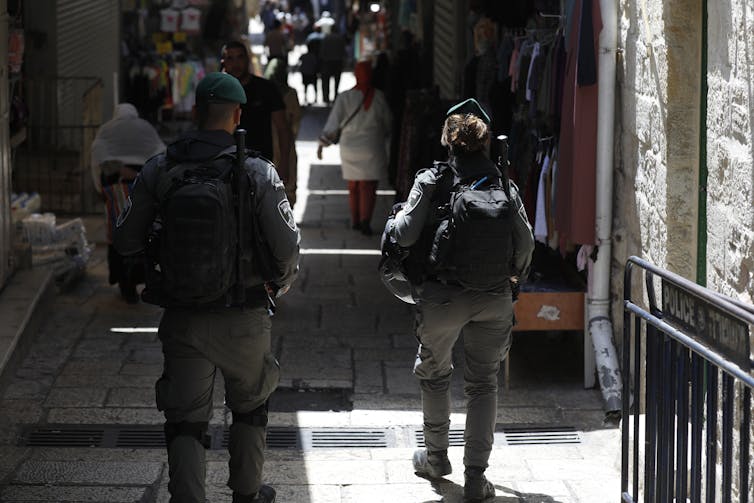 Vue de dos de deux membres des forces frontalières israéliennes patrouillant dans une ruelle de la vieille ville de Jérusalem, avec des civils en arrière-plan
