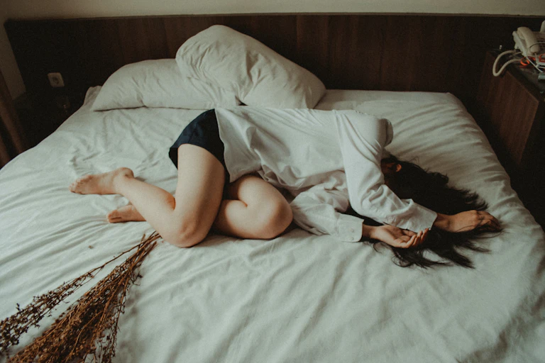 Woman lying on bed heding her head.