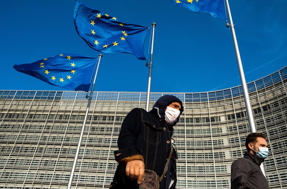 Two people walk in front of the EU headquarters in Brussels. 