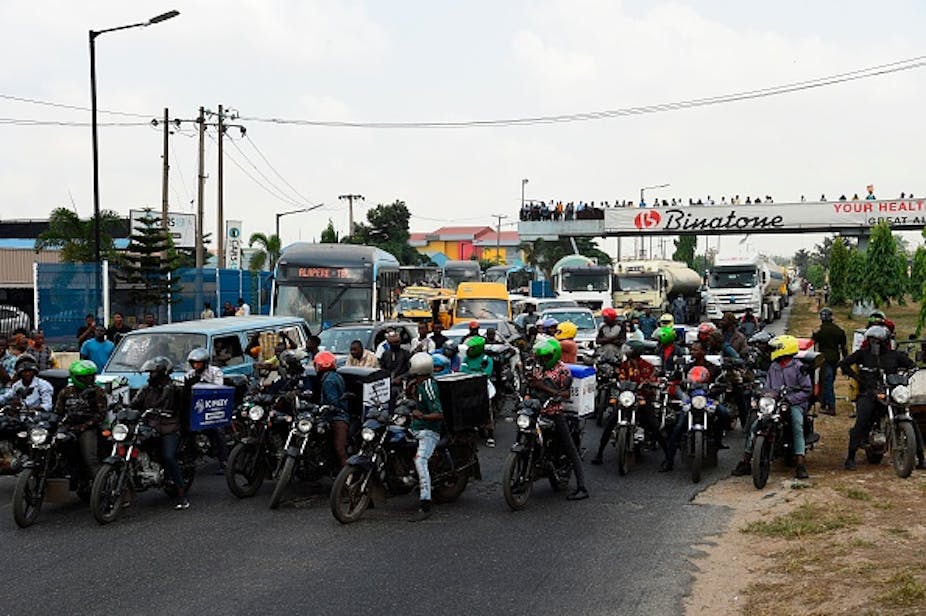 Commercial motorcycle riders in front of vehicular traffic on a road.
