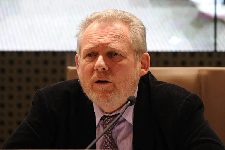 A wearing a suit, shirt and matching tie, speaks speaks at a meeting.tie,