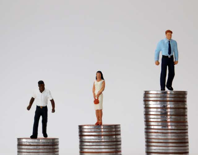 Miniature figures of different races and genders standing on piles of coins of varying heights