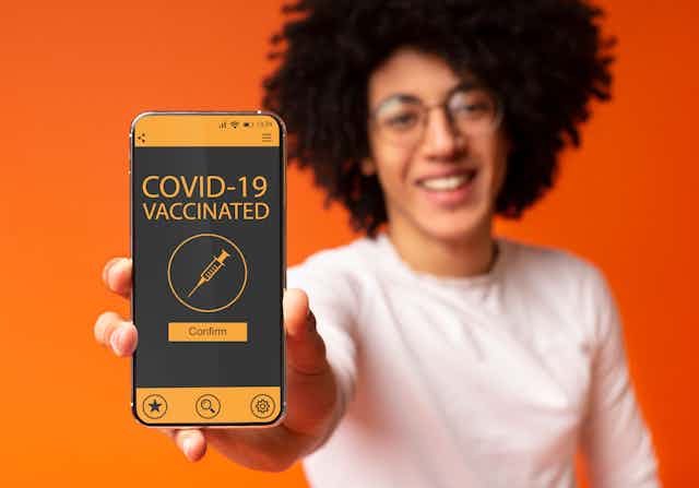 A man holds a smartphone that says 'COVID-19 VACCINATED'.