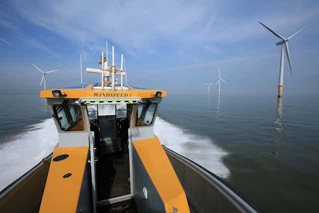 Yellow service boat heads toward offshore wind turbines.