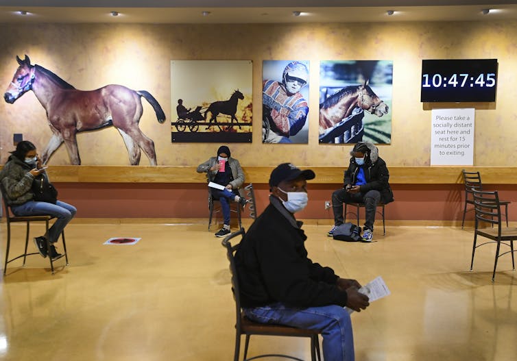 People wait after being vaccinated at the Woodbine Racetrack with images of horses behind them.