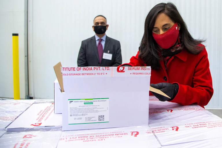 Minister of Public Services Anita Anand wearing a red face mask, opening a box of vaccine.