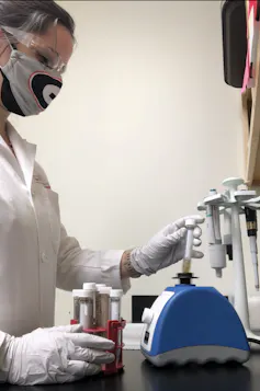 masked scientist holding various test tubes
