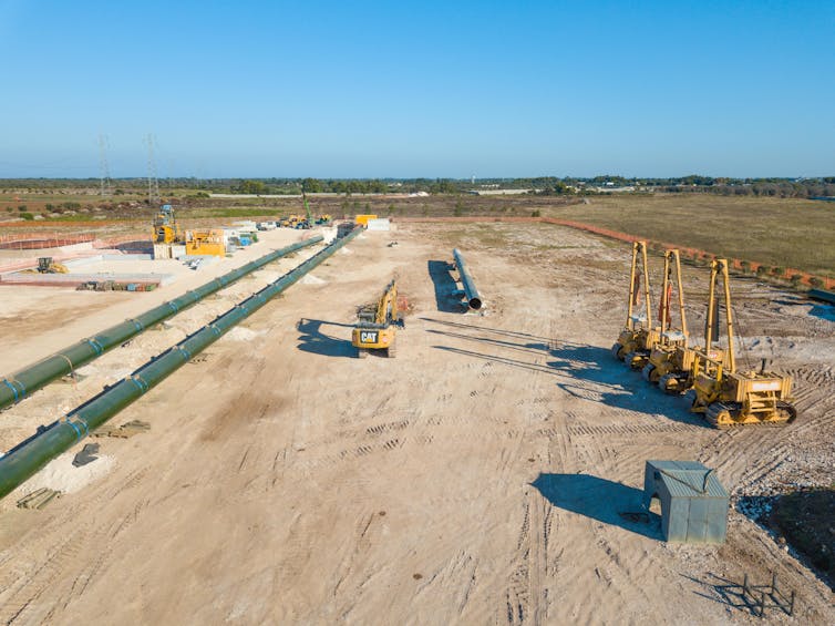 A pipe and diggers on dusty ground