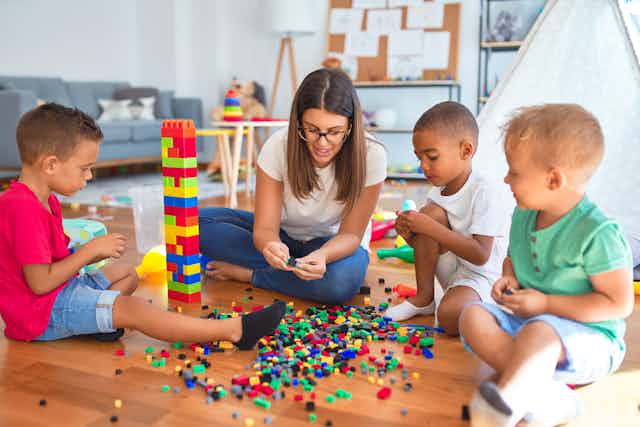Childcare teacher building lego tower with kids.