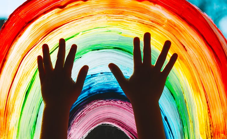 Child's hands in front of a painted rainbow.