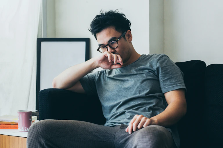 A young man sits on a couch, appears unhappy.