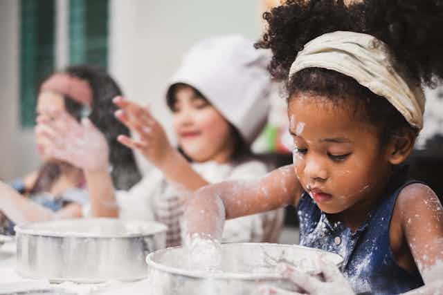 Three little girls covered in flour are mixing cake batter
