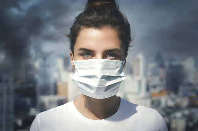 Mujer con mascarilla quirúrgica ante un escenario de contaminación atmosférica.