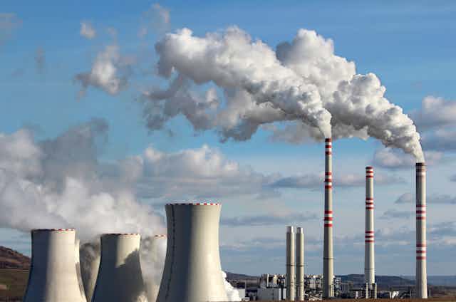 A coal power plant with 3 smoke stacks, emitting smoke