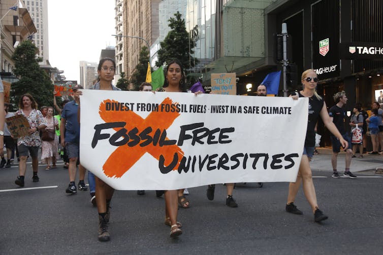 Three protesters carry a sign that reads 'Fossil Free Universities'