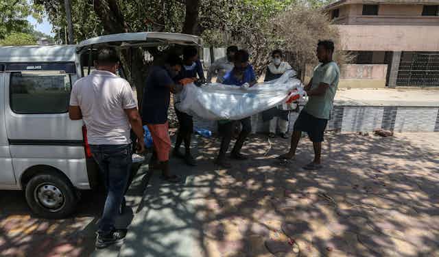 Indian citizens carrying the shrouded body of a COVID victim into the back of a van on the way to a crematorium, Ahmedabad, India, May 11 2021.