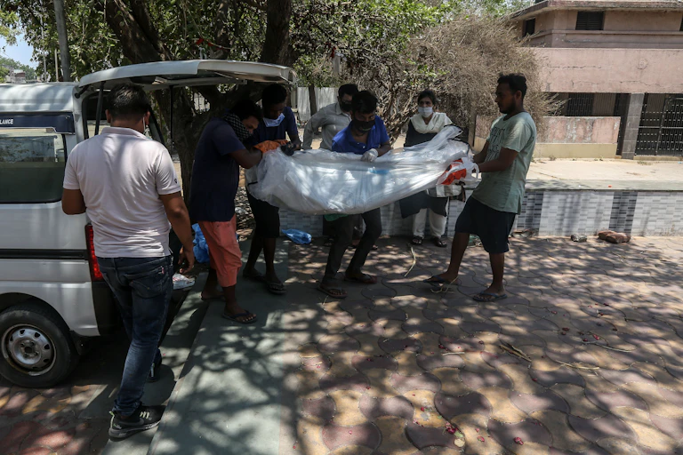 Indian citizens carrying the shrouded body of a COVID victim into the back of a van on the way to a crematorium, Ahmedabad, India, May 11 2021.