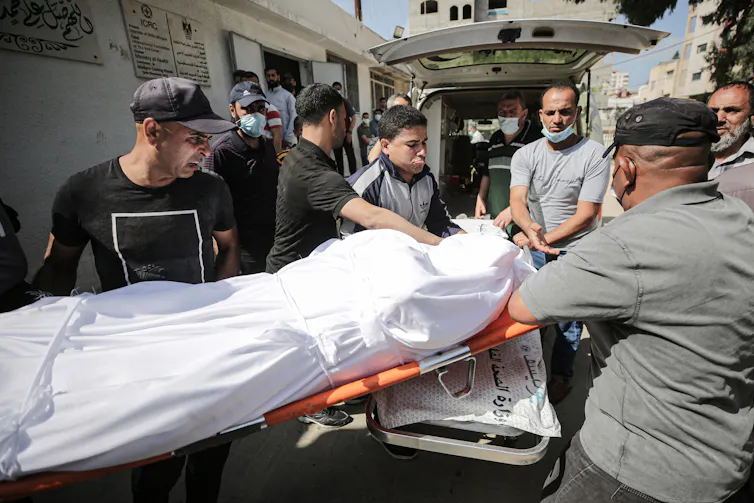 Un grupo de hombres carga un cuerpo envuelto en una sábana en la parte trasera de una ambulancia, en la ciudad de Gaza, mayo de 2021.