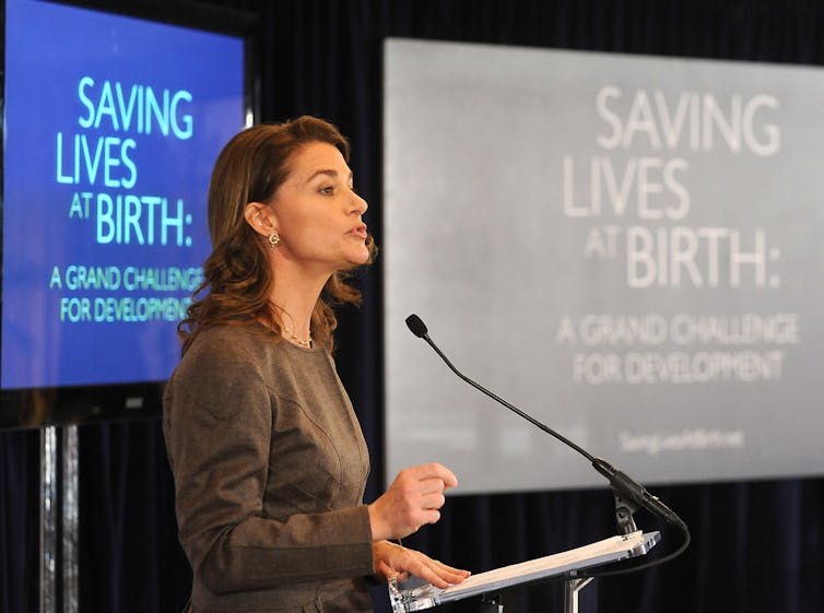 Melinda Gates speaking at a US Agency for International Development event highlighting maternal health initiatives in front of a monitor that says 'saving lives at birth'