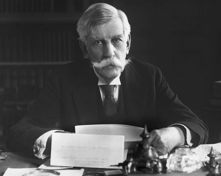 Oliver Wendell Holmes, gray haired and with a big mustache, sitting at a desk.